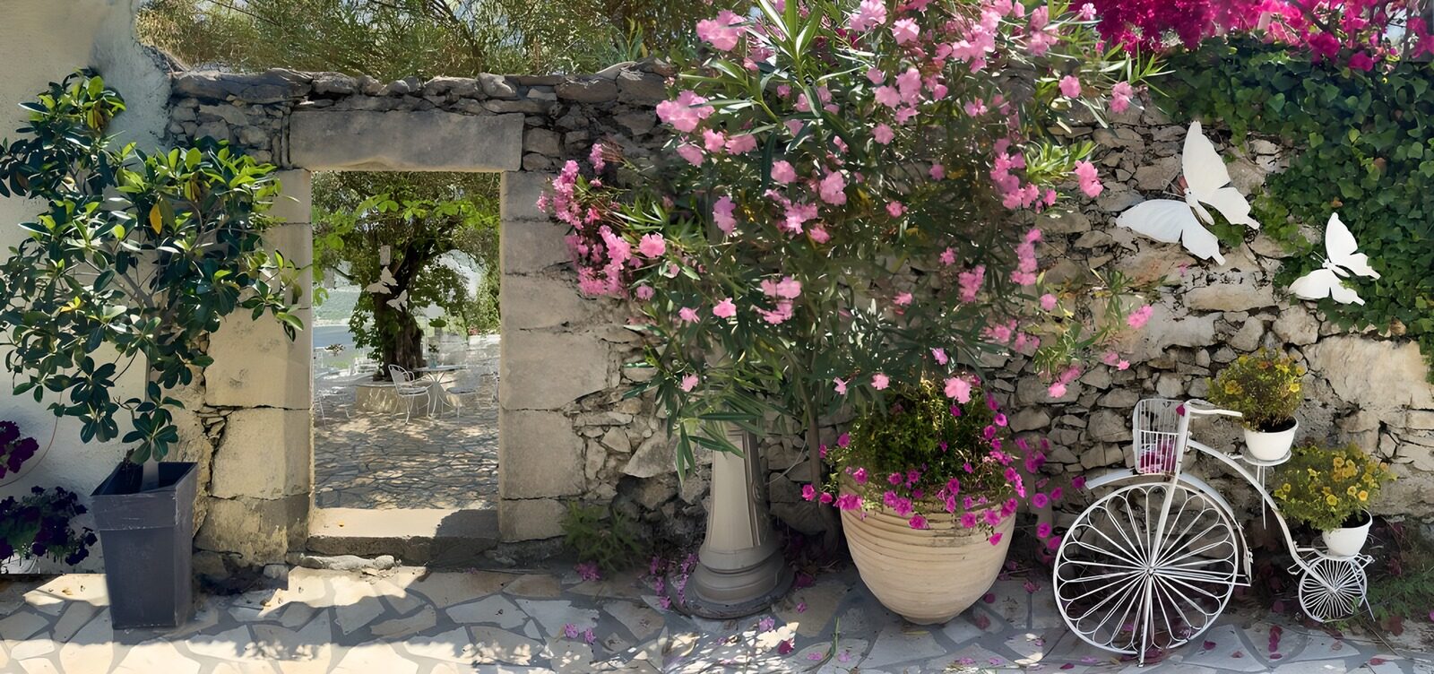 Doorkijk oude muur met doorgang naar patio en oude fiets met bloemen