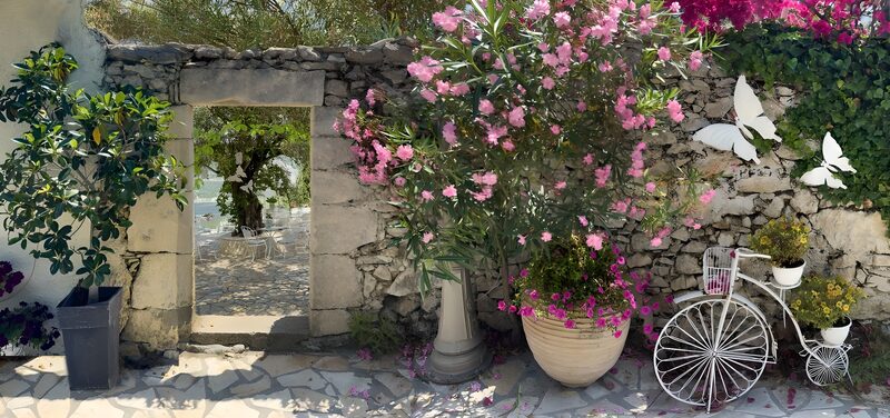 Doorkijk oude muur met doorgang naar patio en oude fiets met bloemen